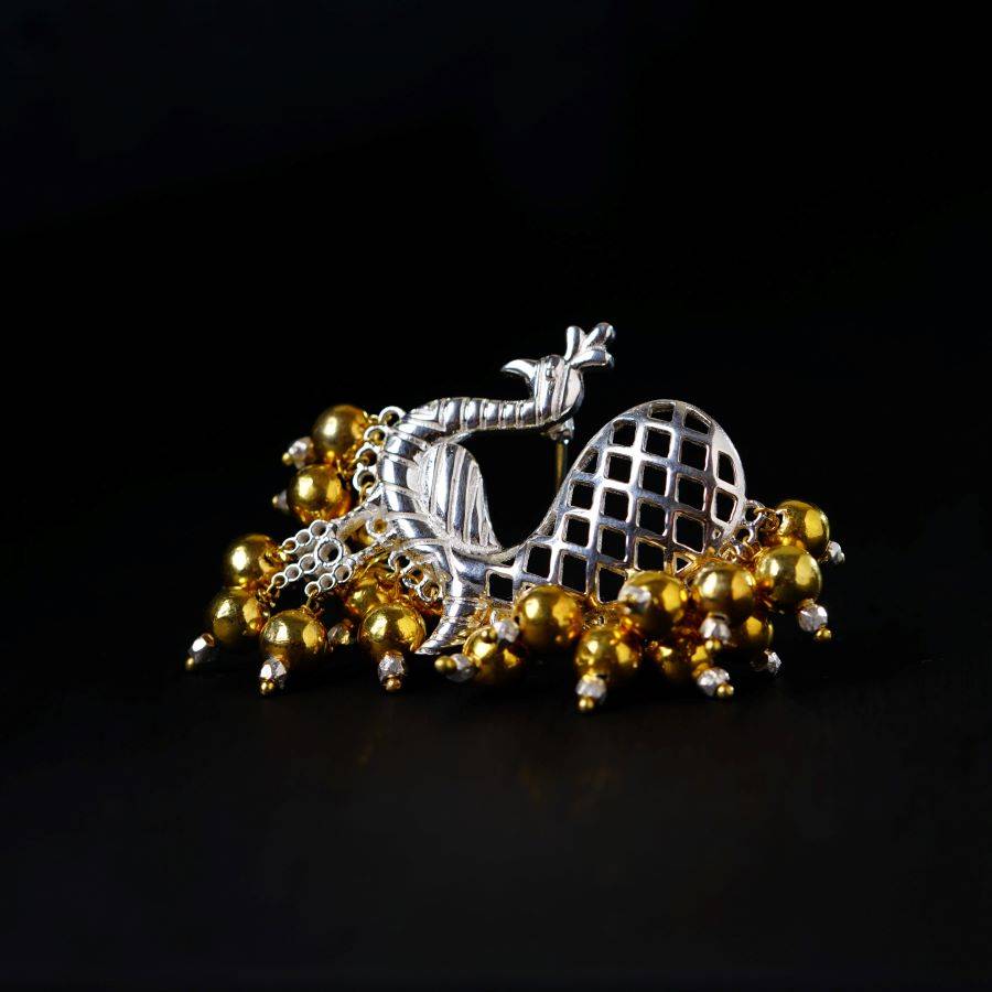 a silver and gold brooch sitting on top of a black surface
