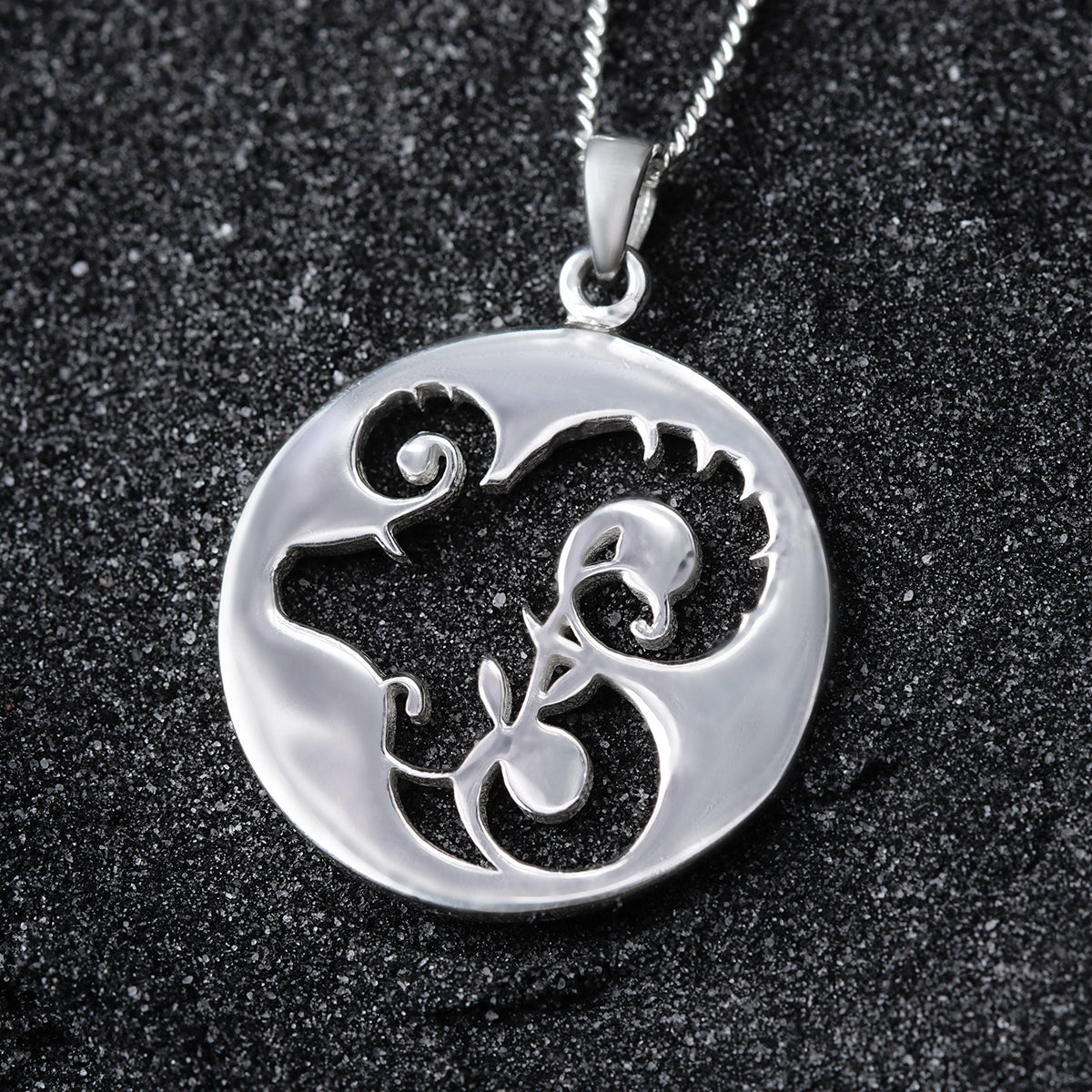 a silver pendant with a swirly design on it