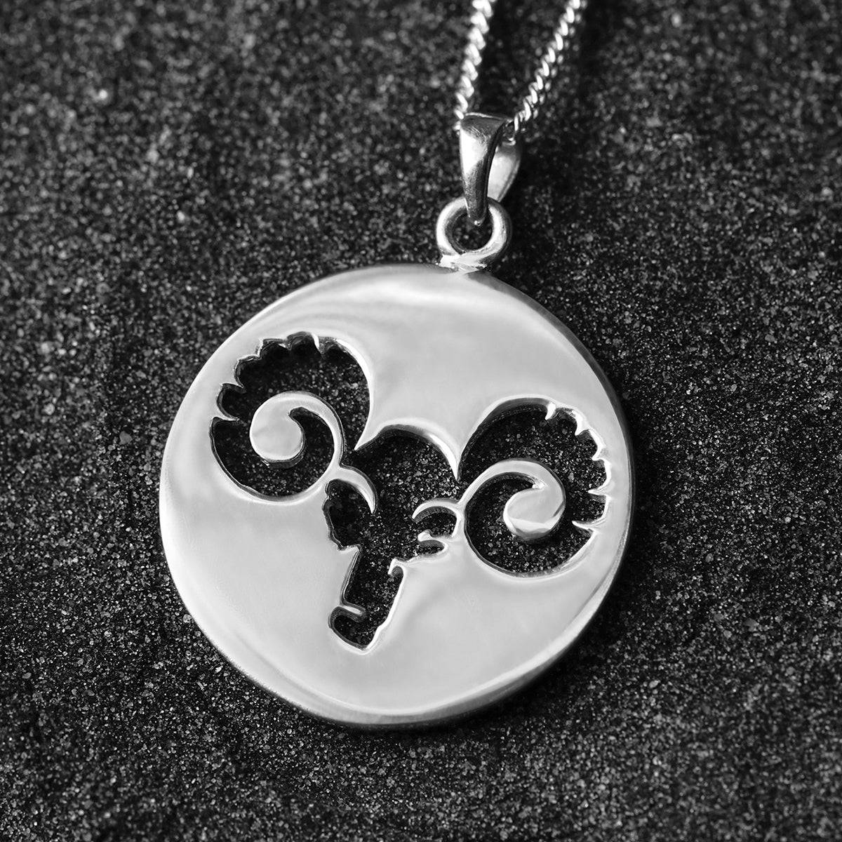 a silver pendant with a black and white image of a ram