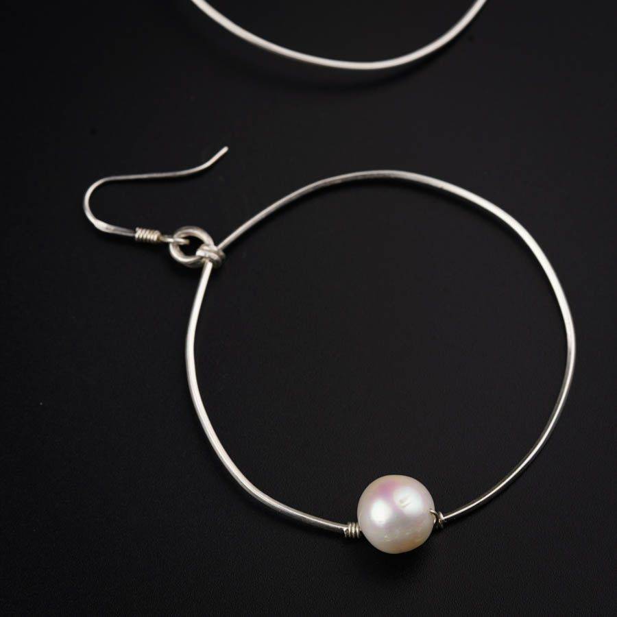 a pair of silver hoop earrings with a white pearl