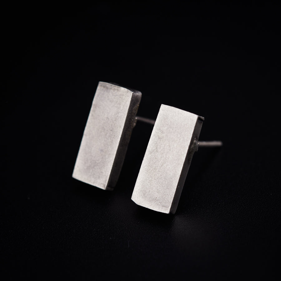 a pair of silver square earrings on a black background
