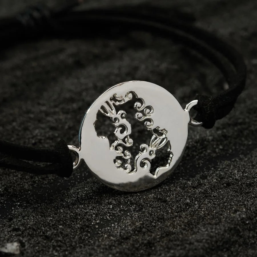 a black cord bracelet with a silver pendant on it