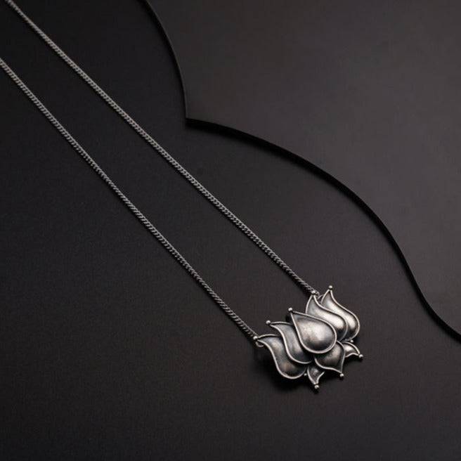 a silver necklace with a flower on a black background