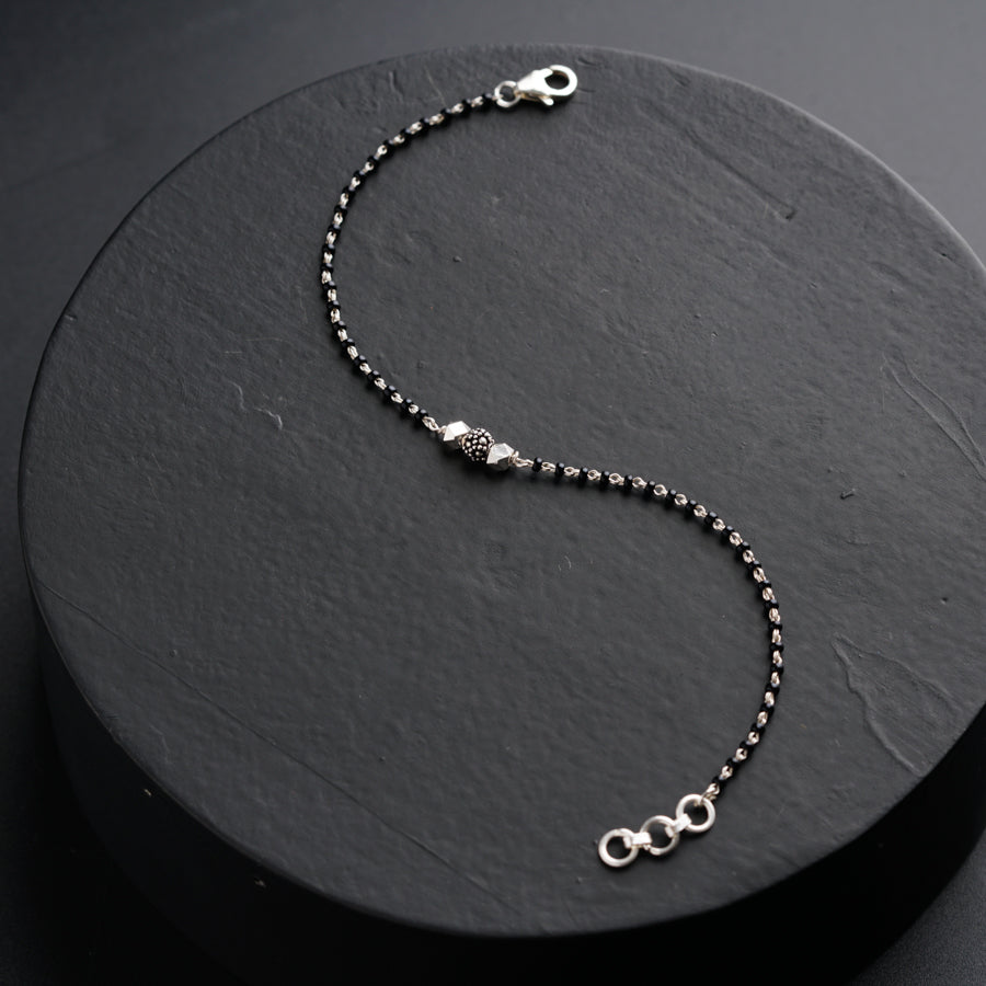 a silver beaded bracelet on a black surface