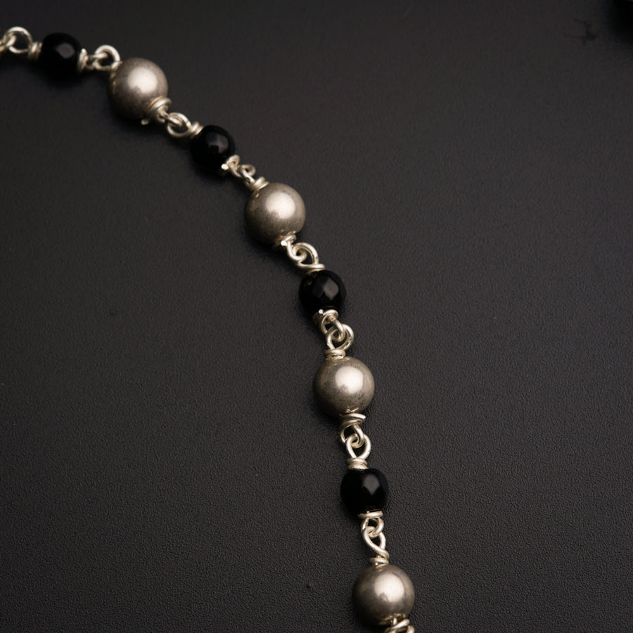 a silver and black beaded necklace on a black surface