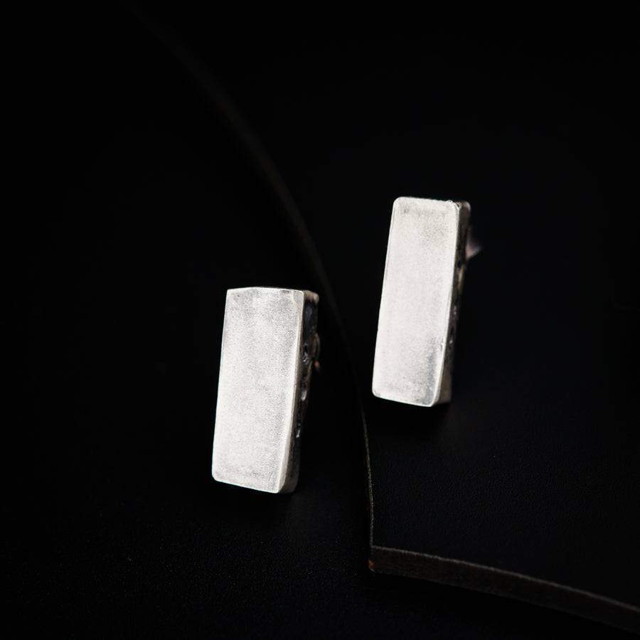a pair of silver square earrings on a black surface