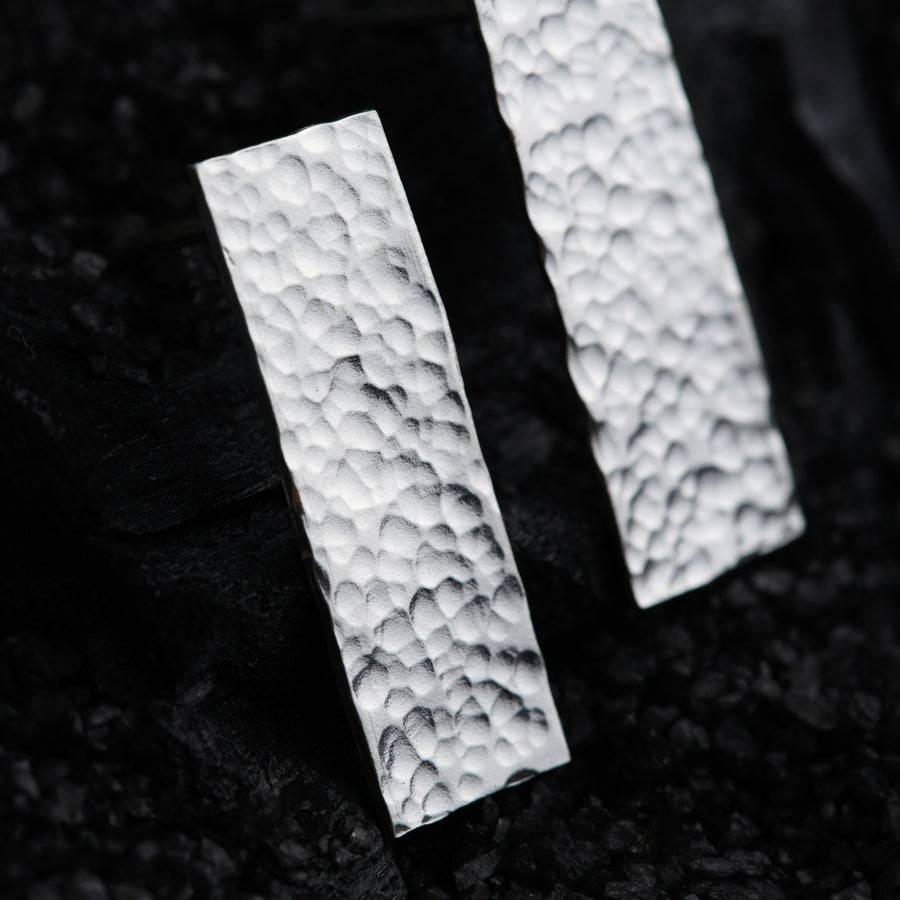 a pair of silver earrings sitting on top of a black surface