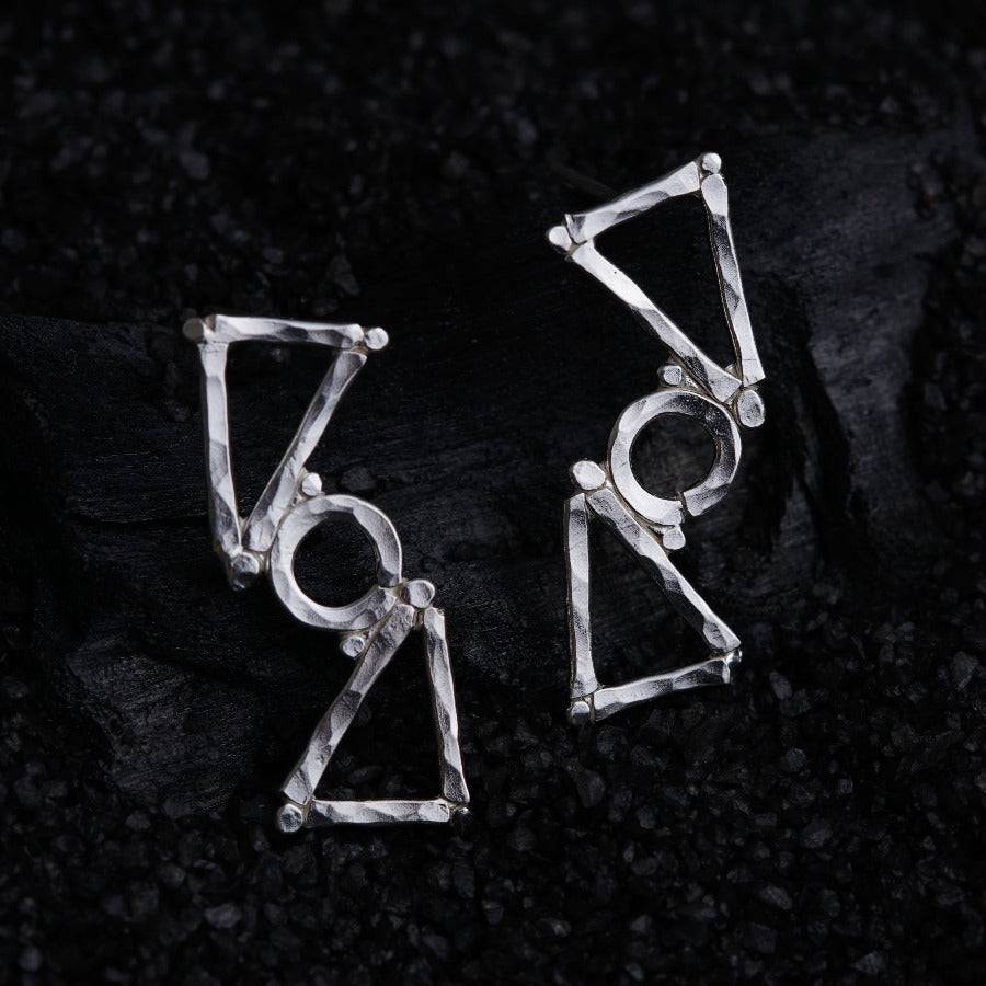 a pair of triangle shaped earrings sitting on top of a black surface