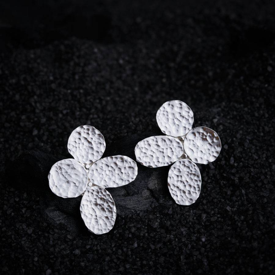 a pair of silver flower earrings on a black surface