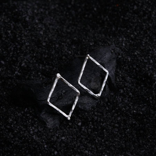 a pair of square earrings sitting on top of a black surface