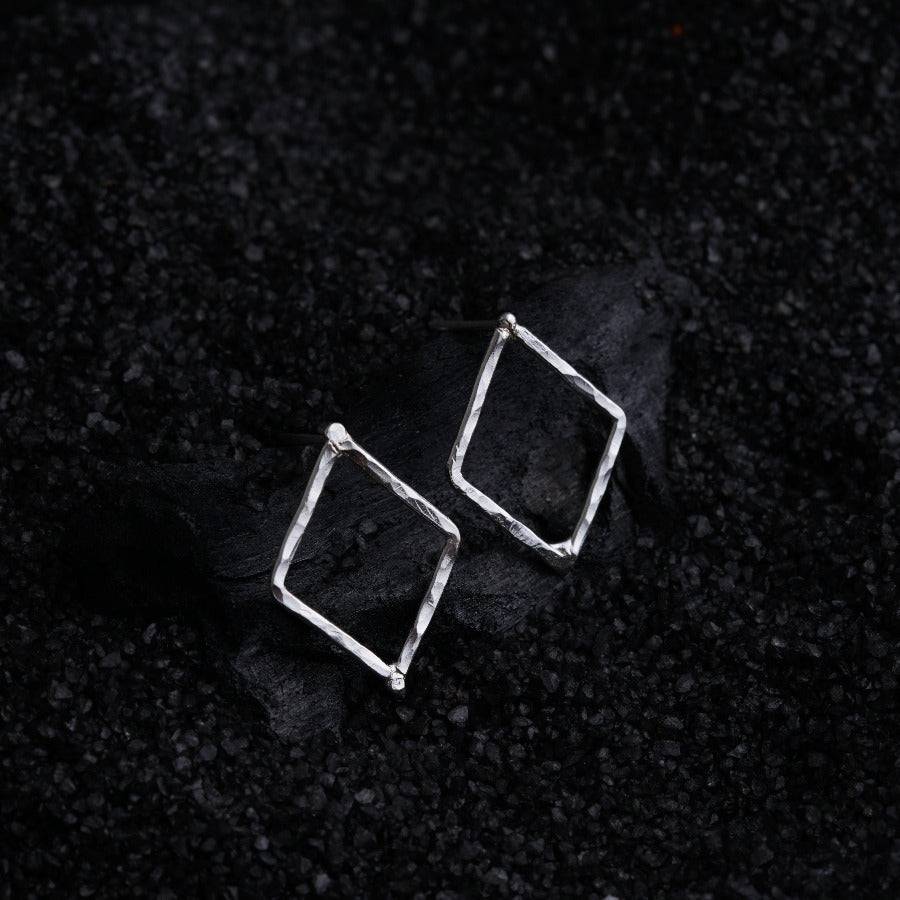 a pair of square earrings sitting on top of a black surface