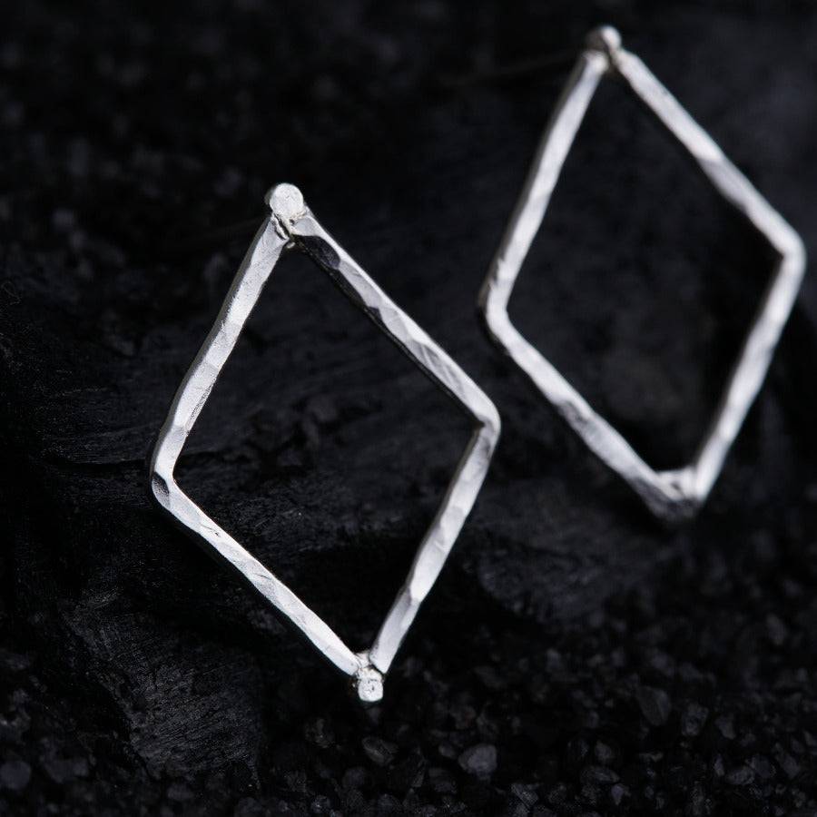a pair of silver square earrings on a black surface