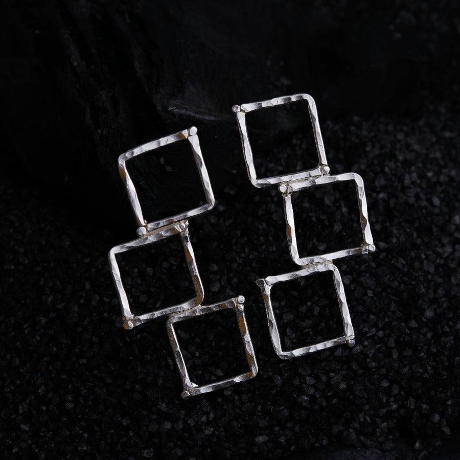 a set of four square silver earrings on a black surface