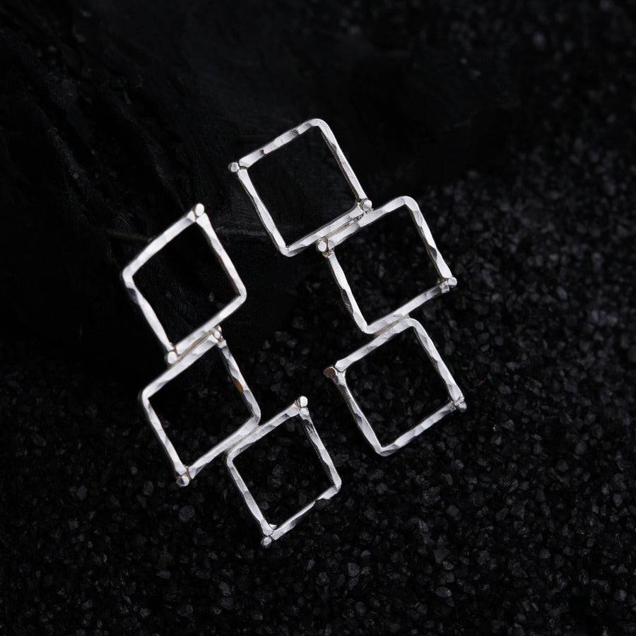 three square shaped silver earrings on a black surface