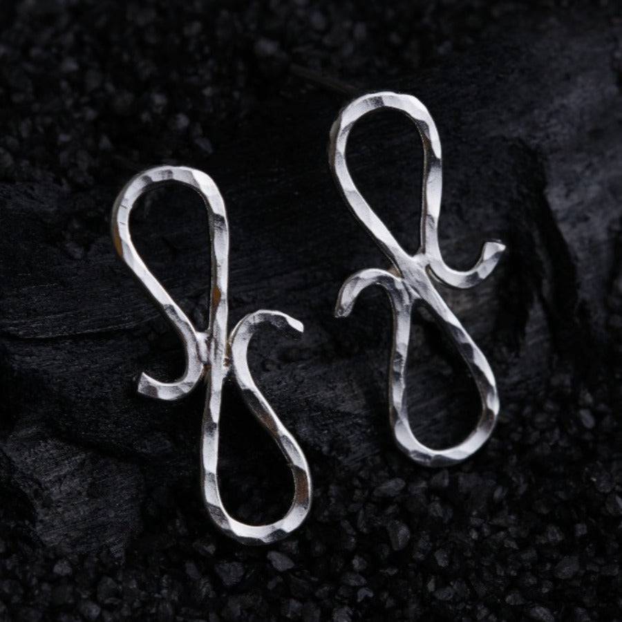 a pair of silver earrings sitting on top of a black surface