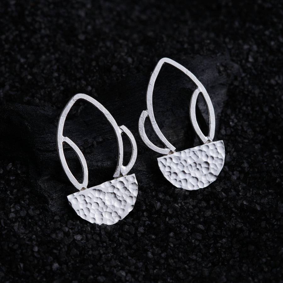 a pair of silver earrings sitting on top of a black surface