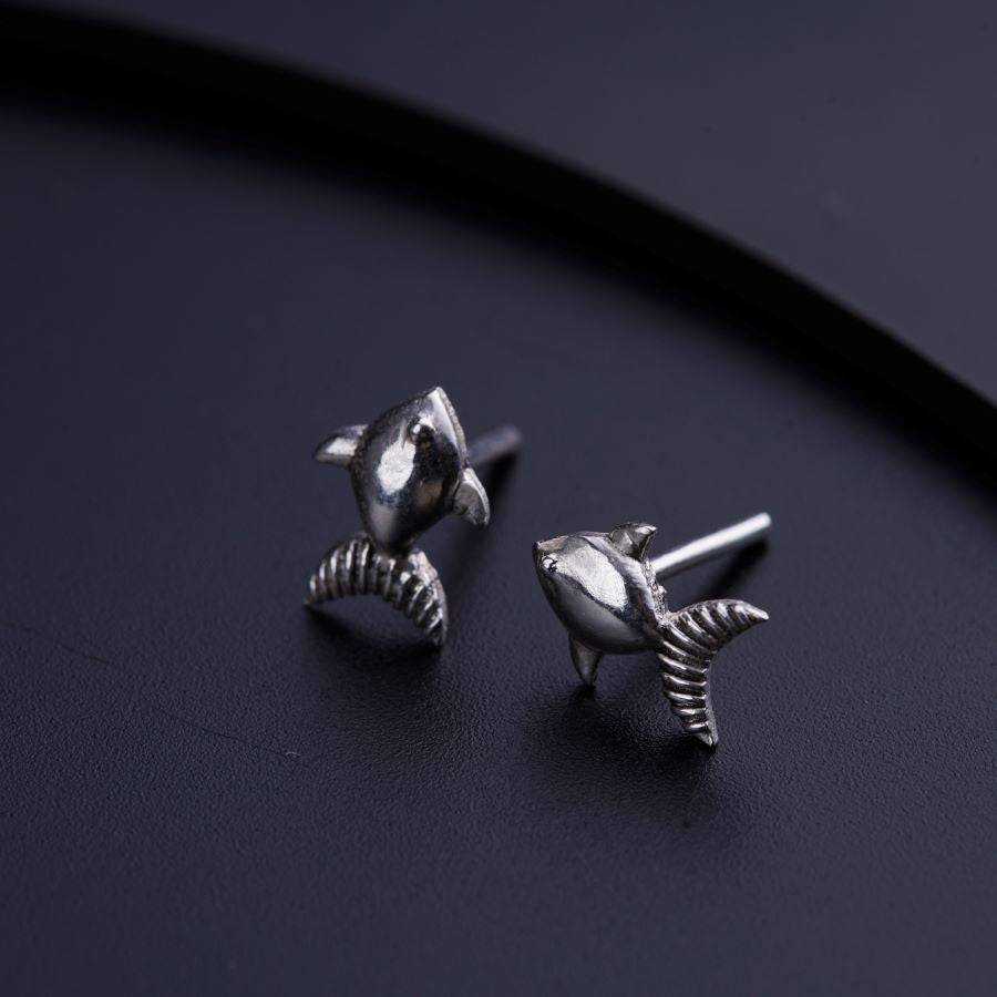 a pair of silver dolphin earrings sitting on top of a table