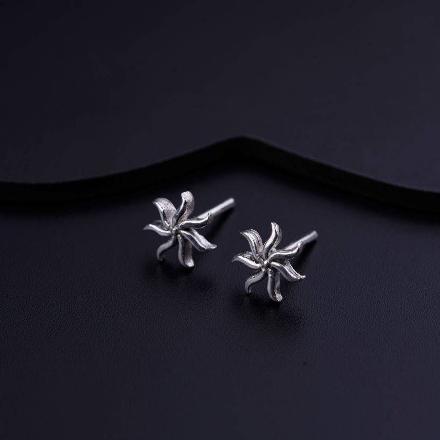 a pair of silver flower earrings on a black background
