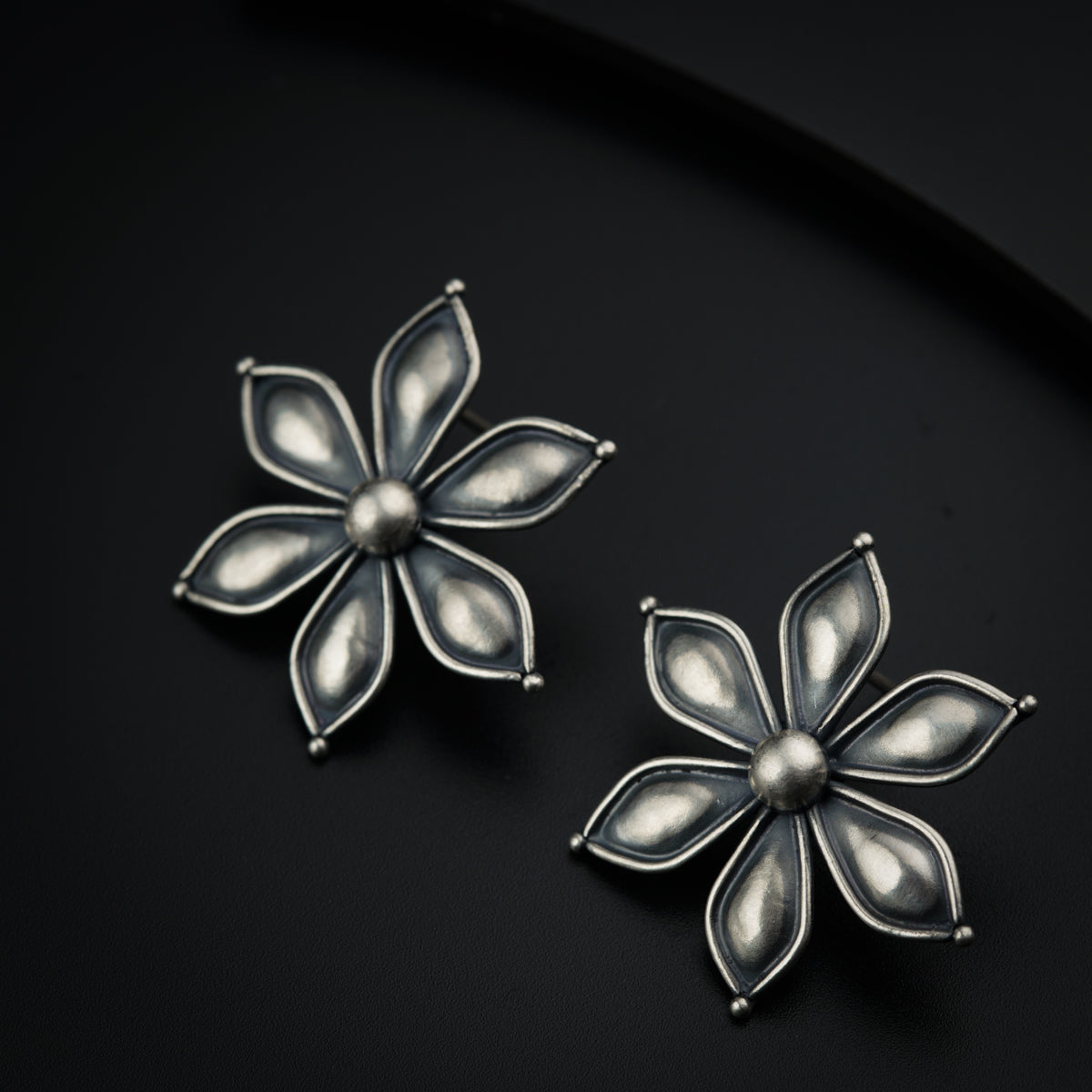 a pair of flower shaped earrings on a black surface
