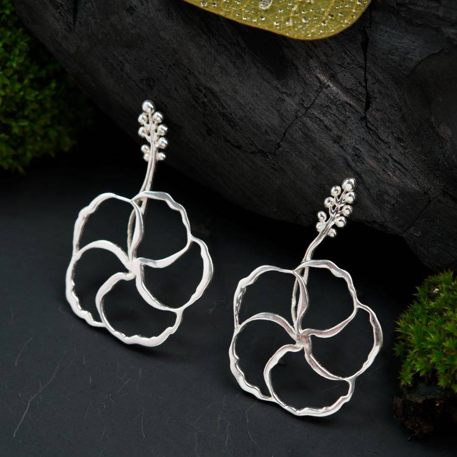 a pair of silver flower earrings on a black surface