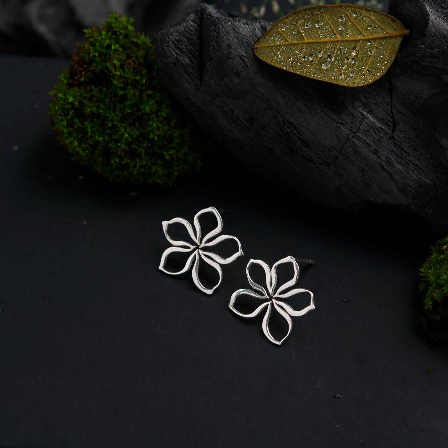 a pair of silver flower earrings sitting on top of a black surface