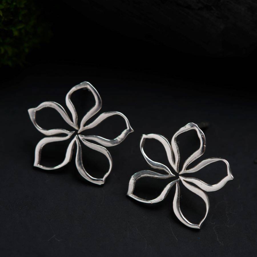 a pair of silver flower earrings on a black surface