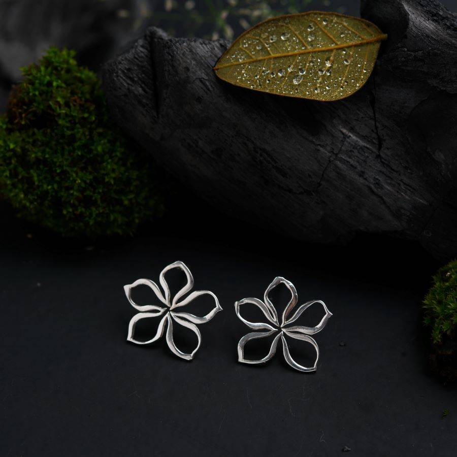 a pair of silver flower earrings sitting on top of a black surface