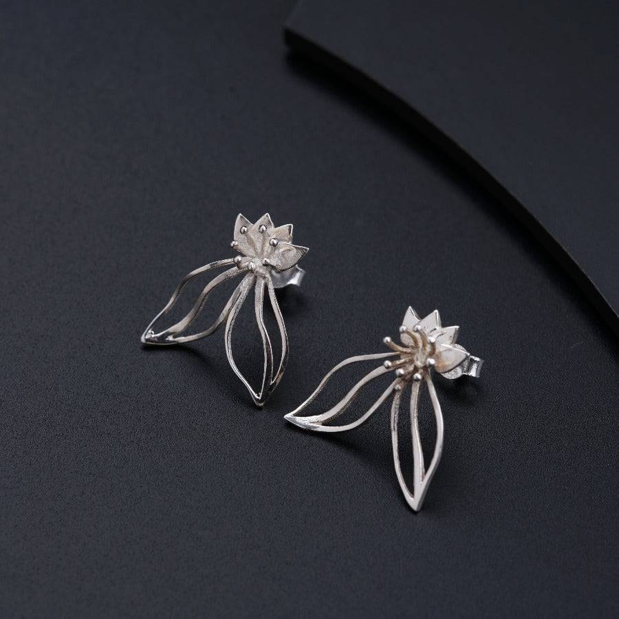 a pair of silver flower earrings on a black surface