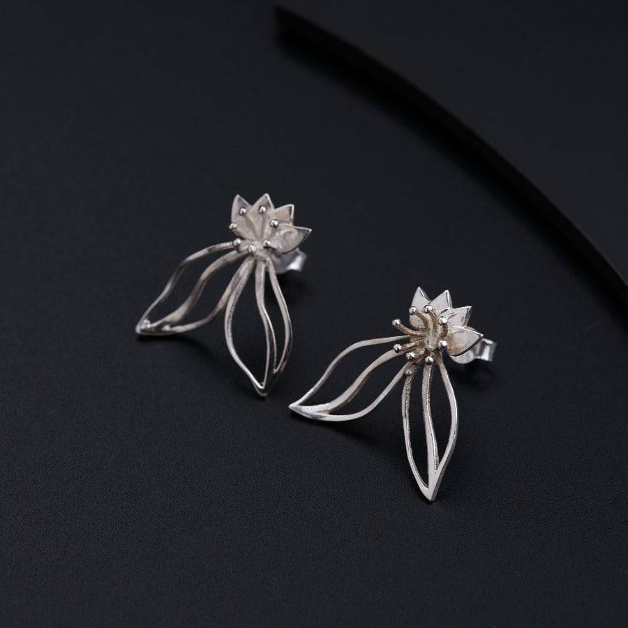 a pair of silver flower earrings on a black surface