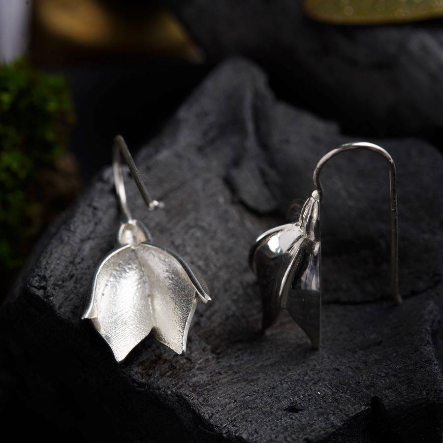 a pair of silver earrings sitting on top of a rock