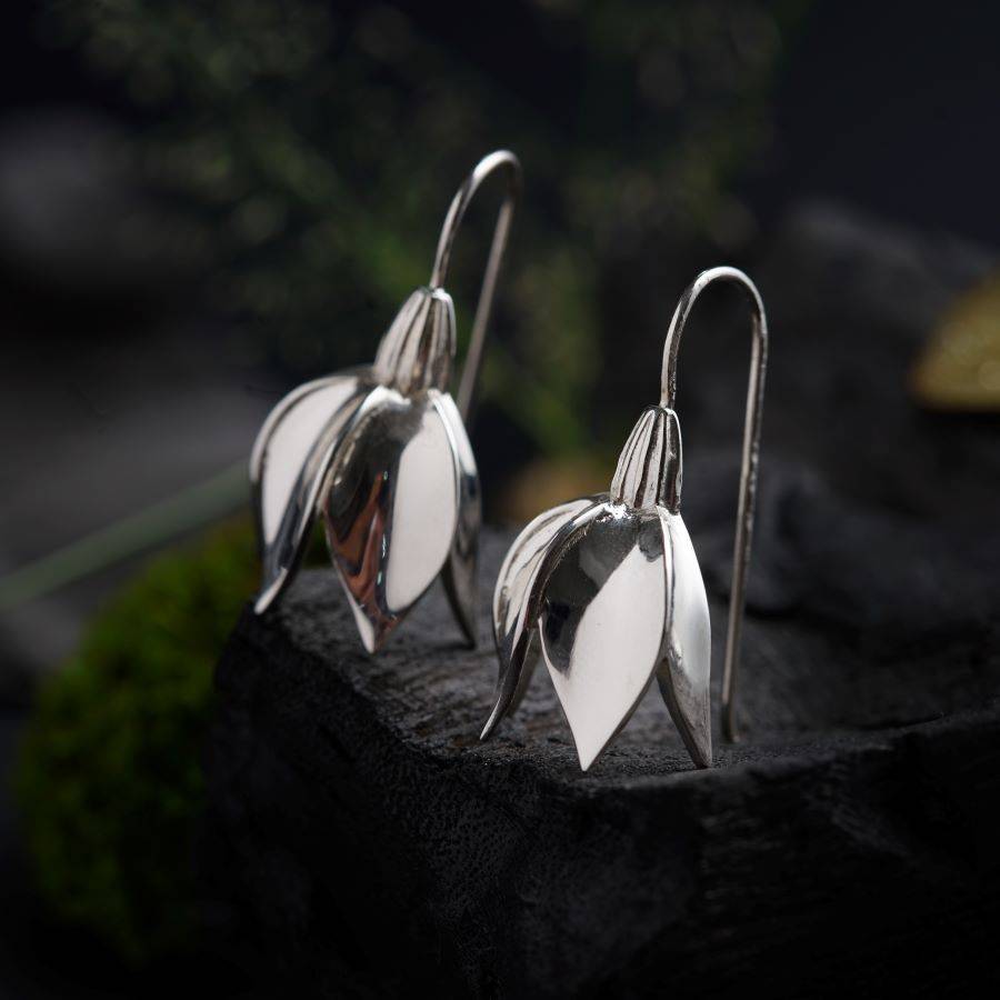 a pair of silver earrings sitting on top of a rock