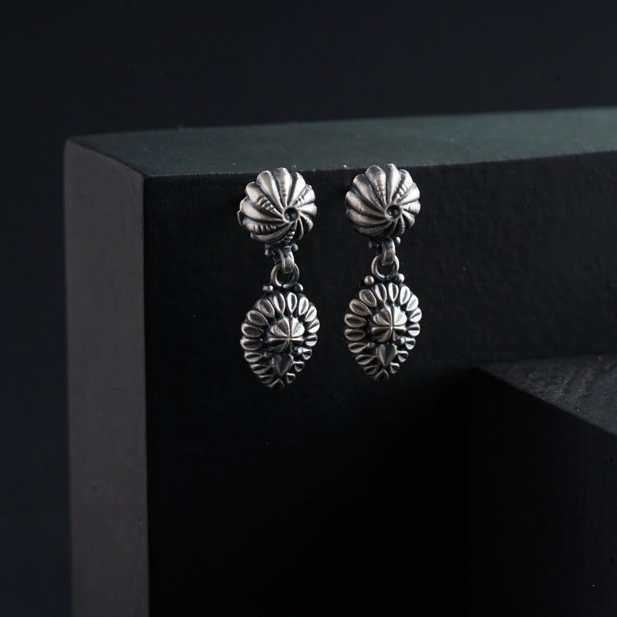 a pair of silver earrings sitting on top of a black box