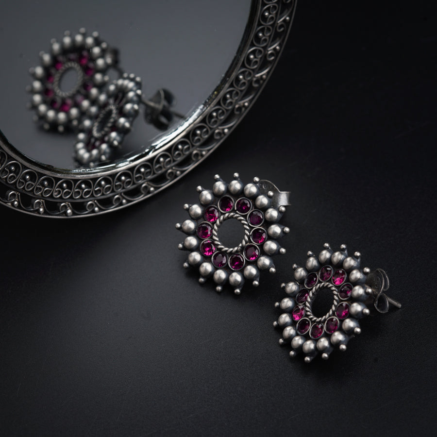 a pair of pink and silver earrings sitting next to a mirror