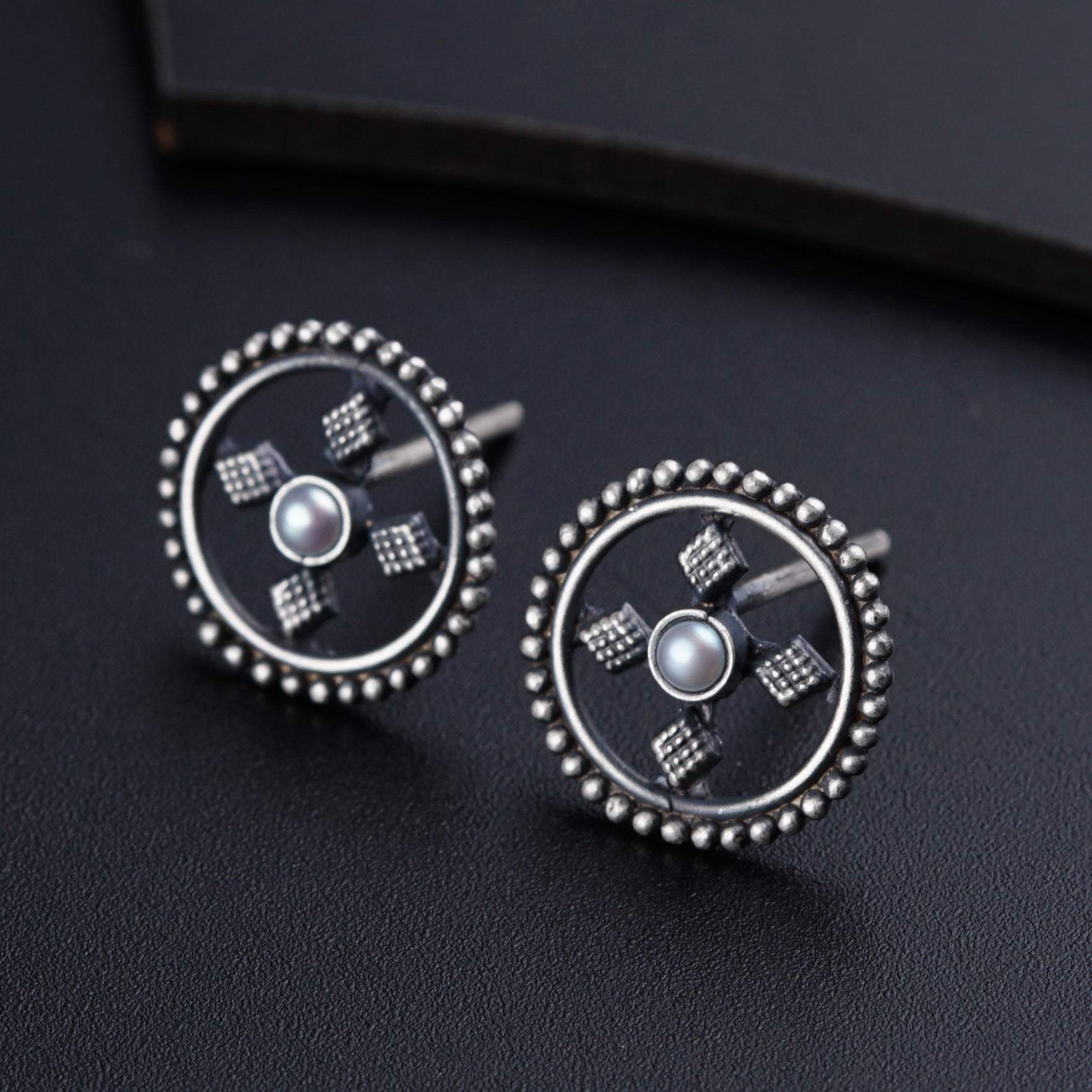a pair of silver earrings with pearls on a black surface