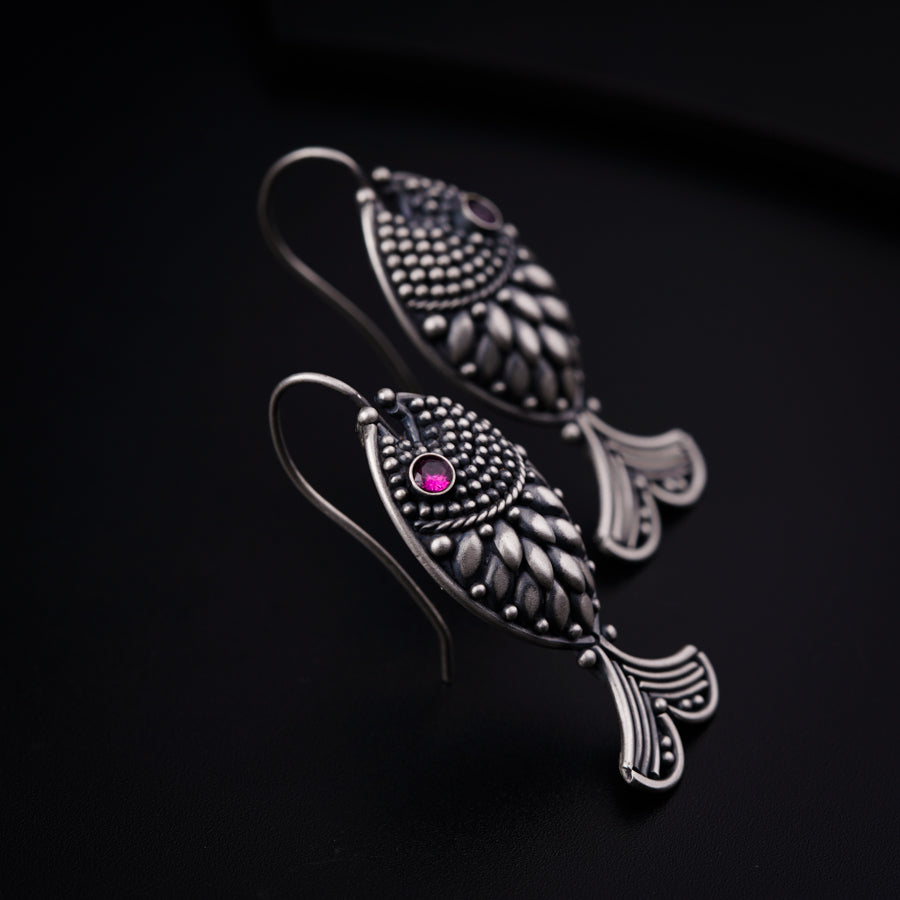 a pair of fish shaped earrings with a pink stone