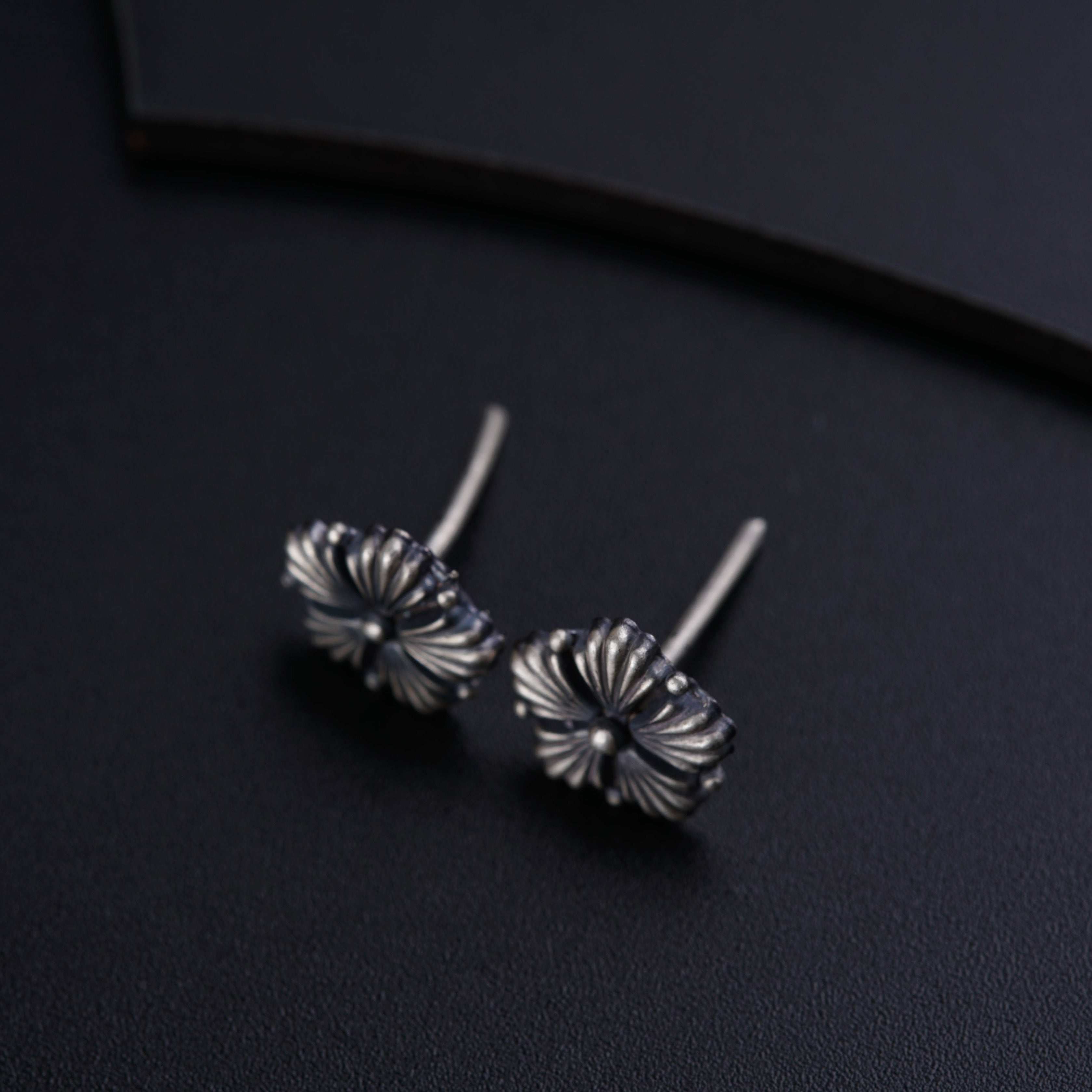 a pair of silver earrings sitting on top of a black surface