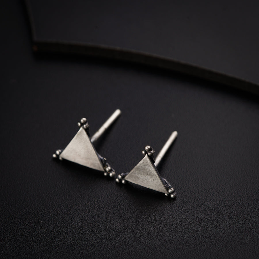 a pair of triangle shaped earrings on a black surface