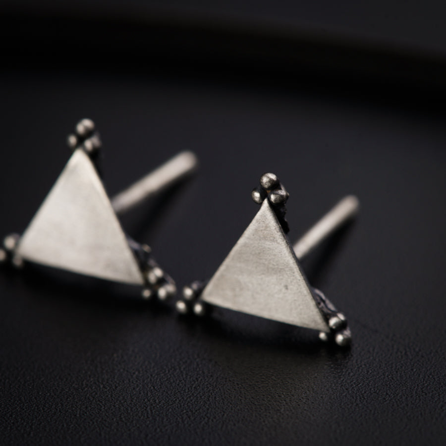 a pair of triangle shaped earrings on a black surface
