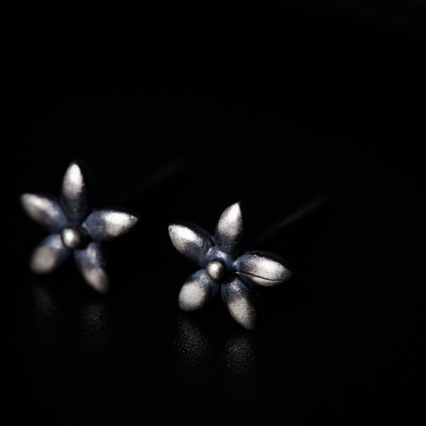 a pair of silver flower earrings on a black surface