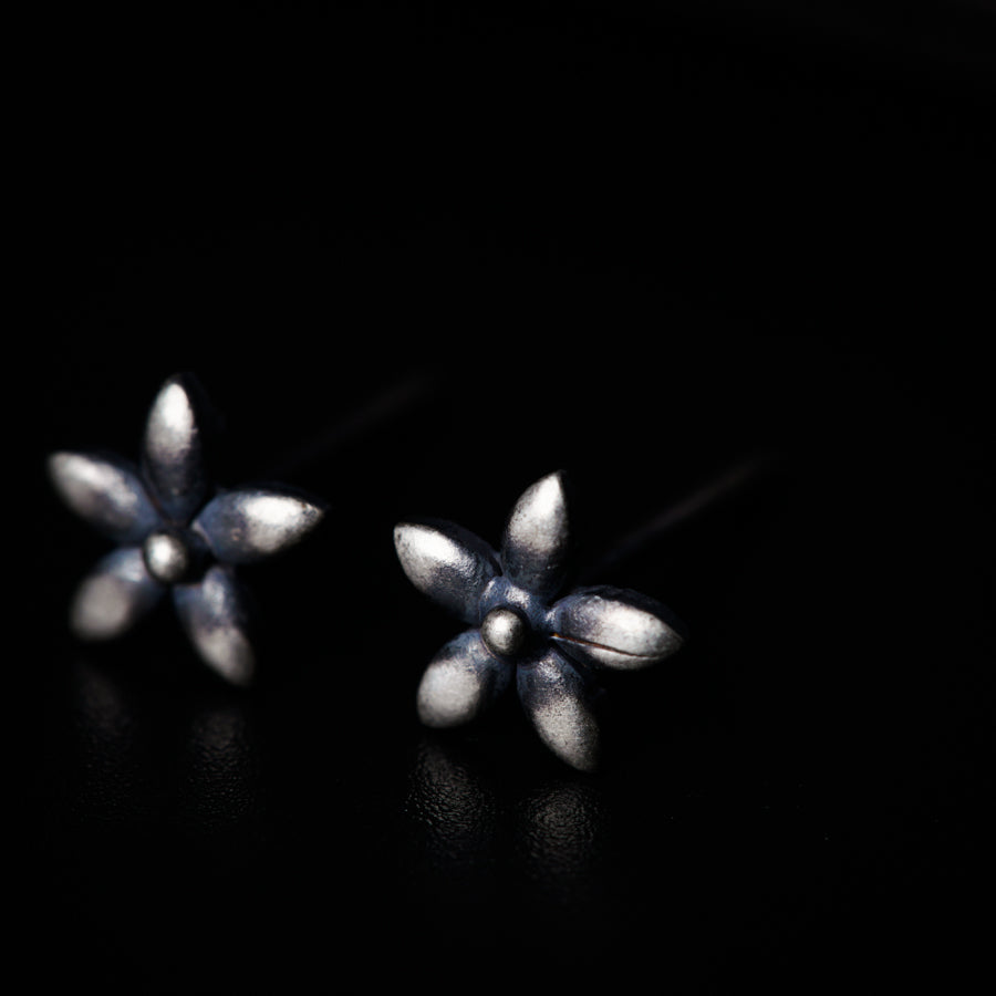 a pair of silver flower earrings on a black surface