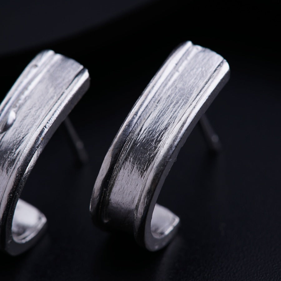 a pair of silver earrings sitting on top of a black surface