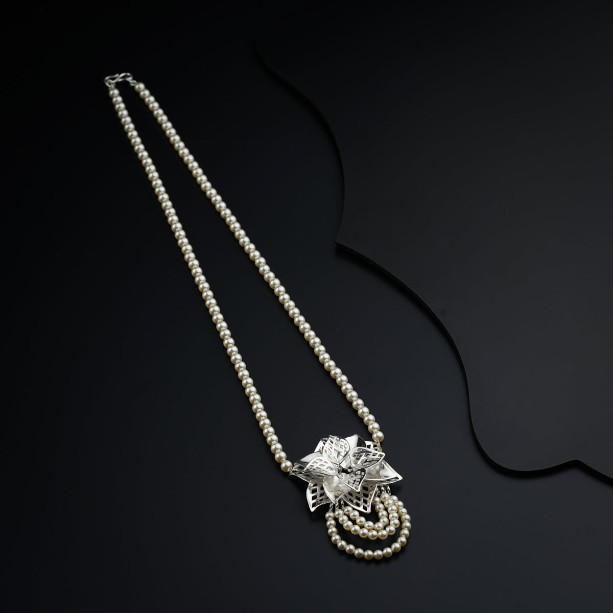 a white pearl necklace with a silver flower on it