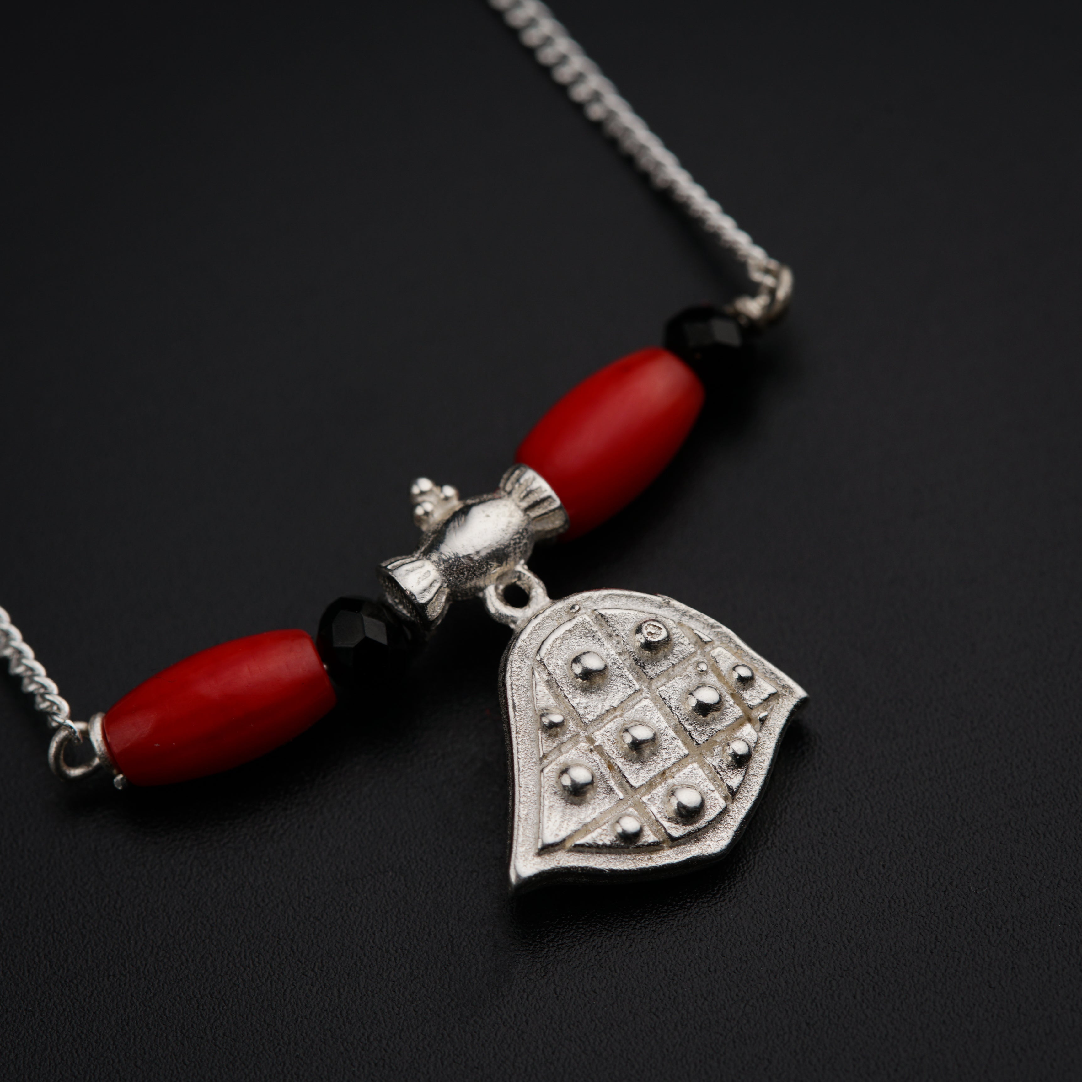 a red beaded necklace with a silver hamsa pendant