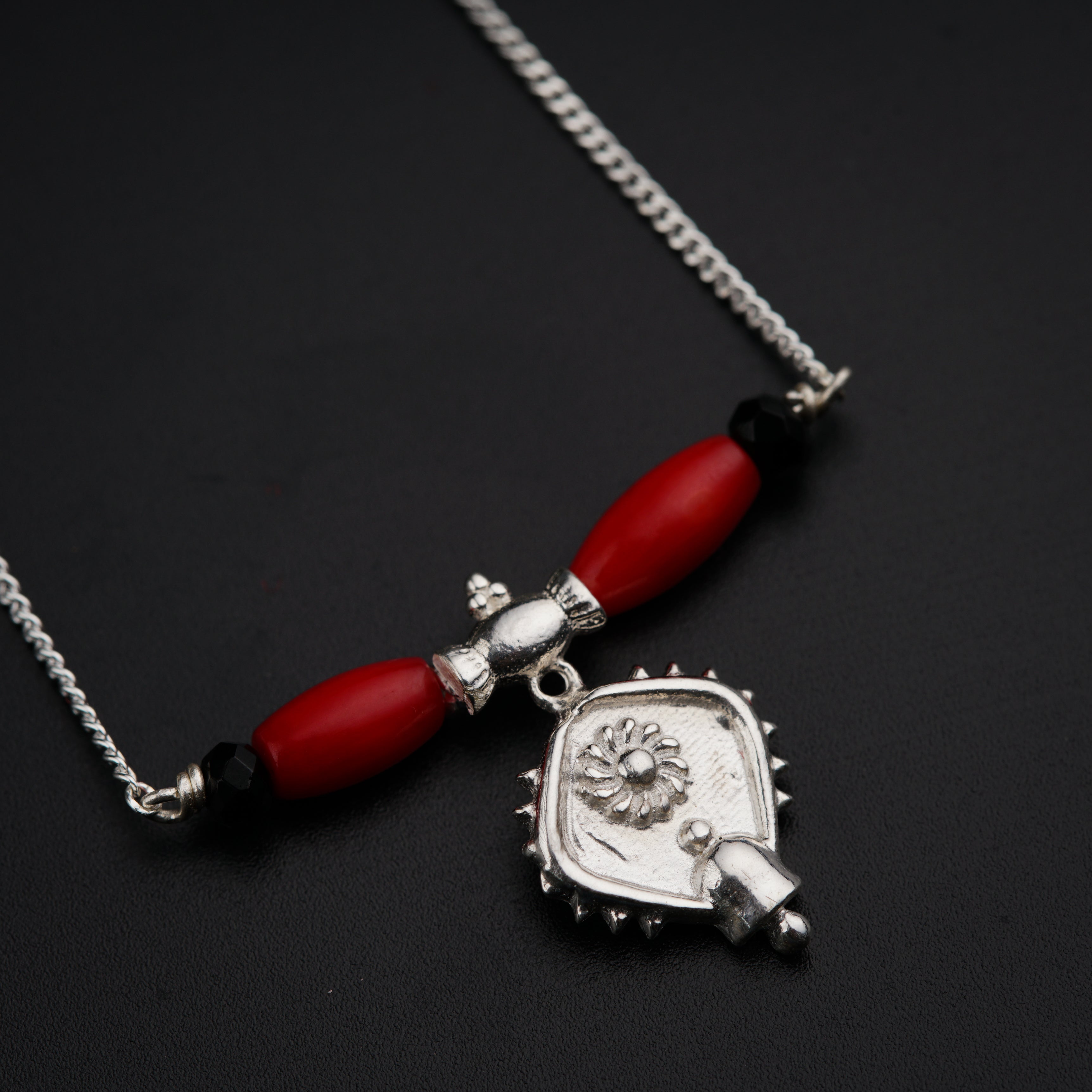 a necklace with a red bead and a silver pendant