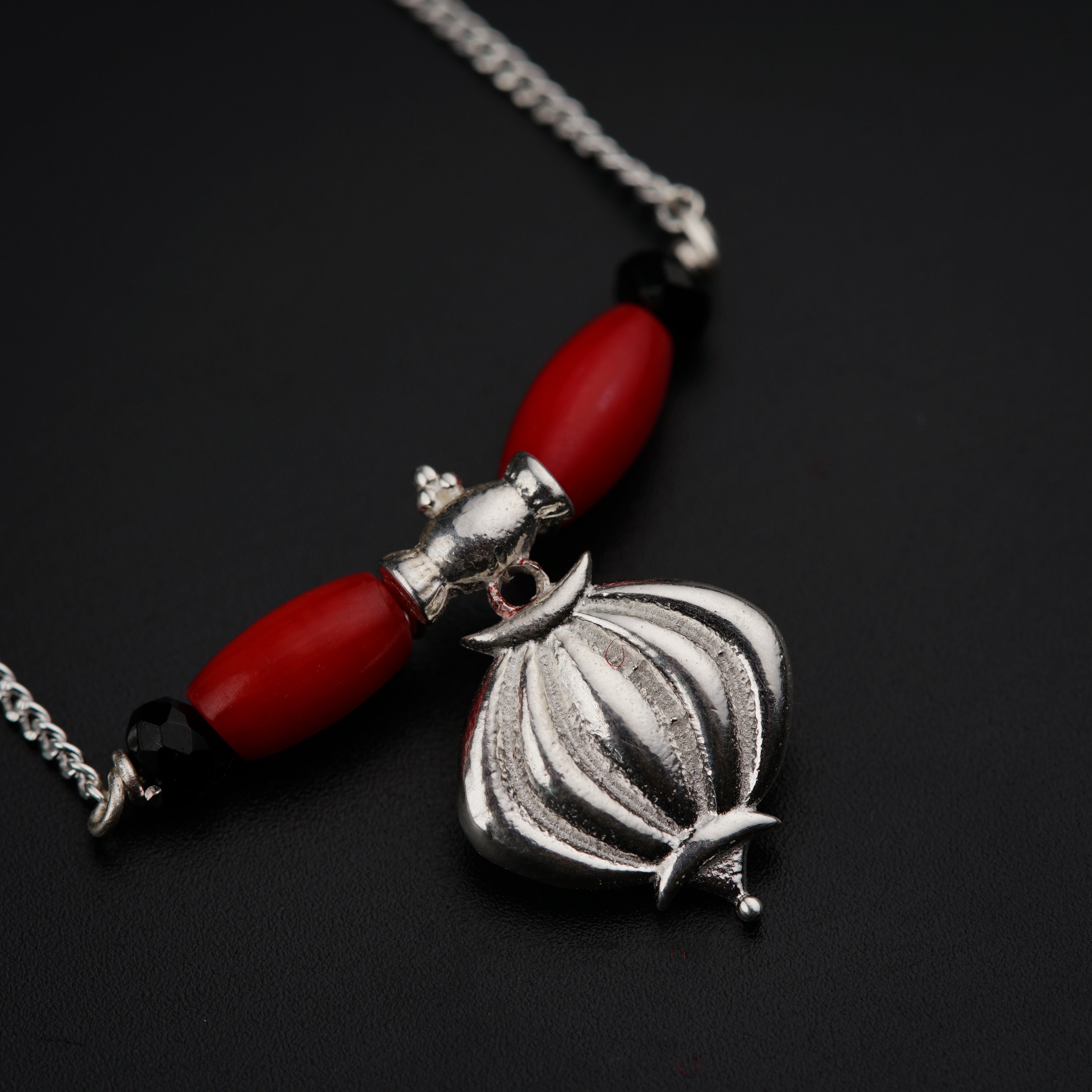 a necklace with a red bead and a silver pendant