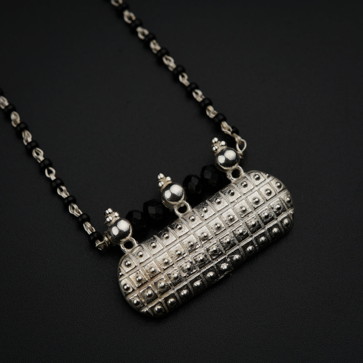 a necklace with a silver object on a black background