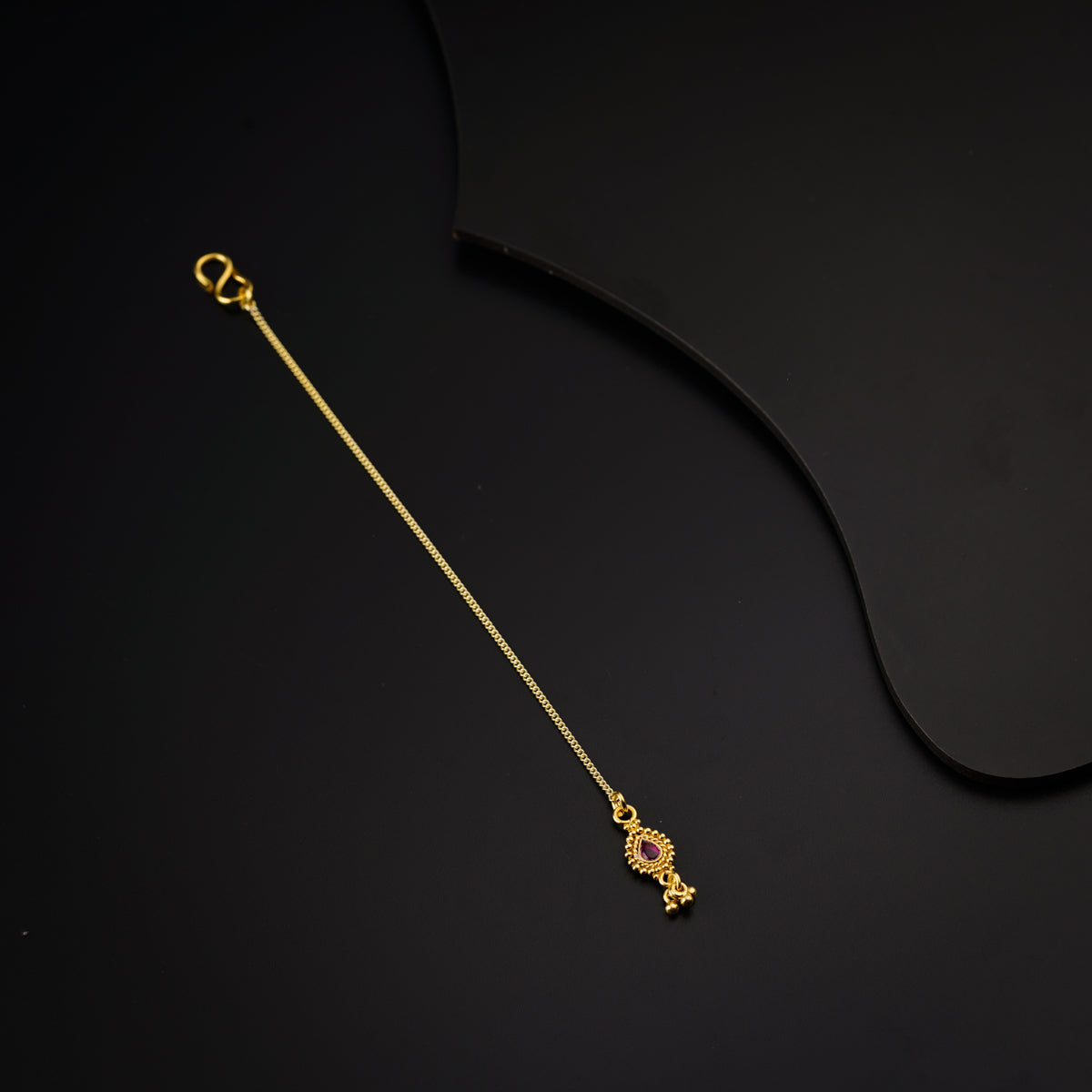 a gold necklace with a pink stone on a black background