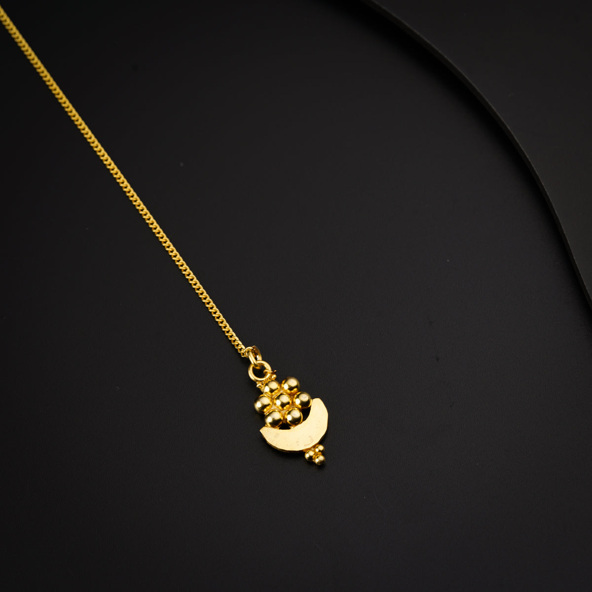 a gold plated necklace with a small pendant on a black surface