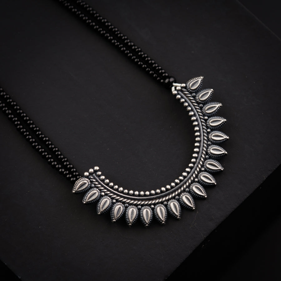 a silver necklace with leaves on a black background