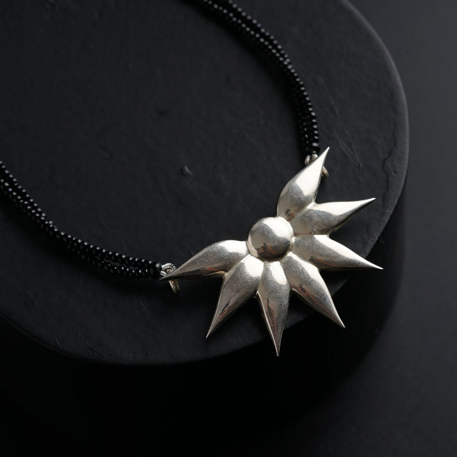 a black necklace with a silver flower on it